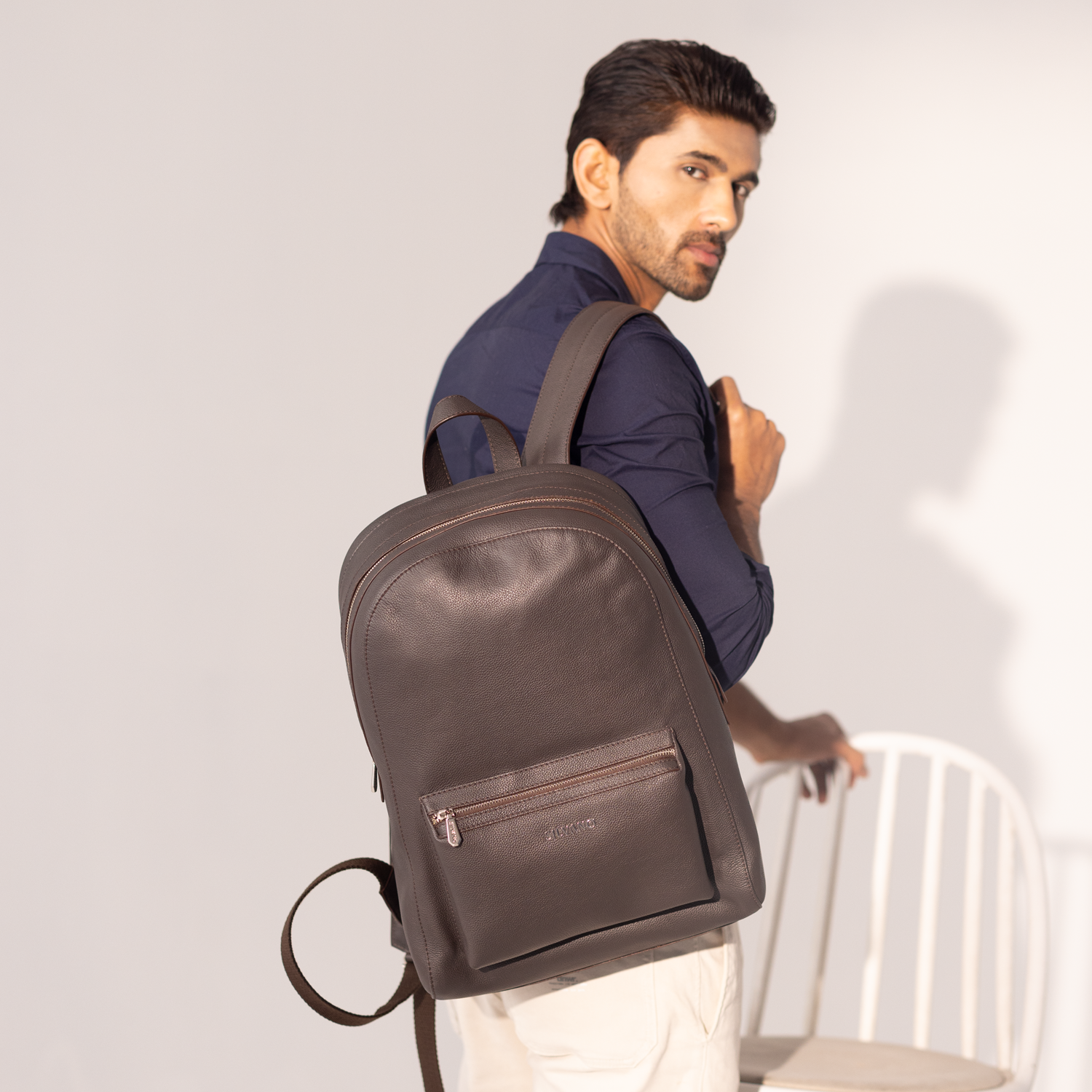 dark brown leather backpack styled by man in navy shirt and cream pants