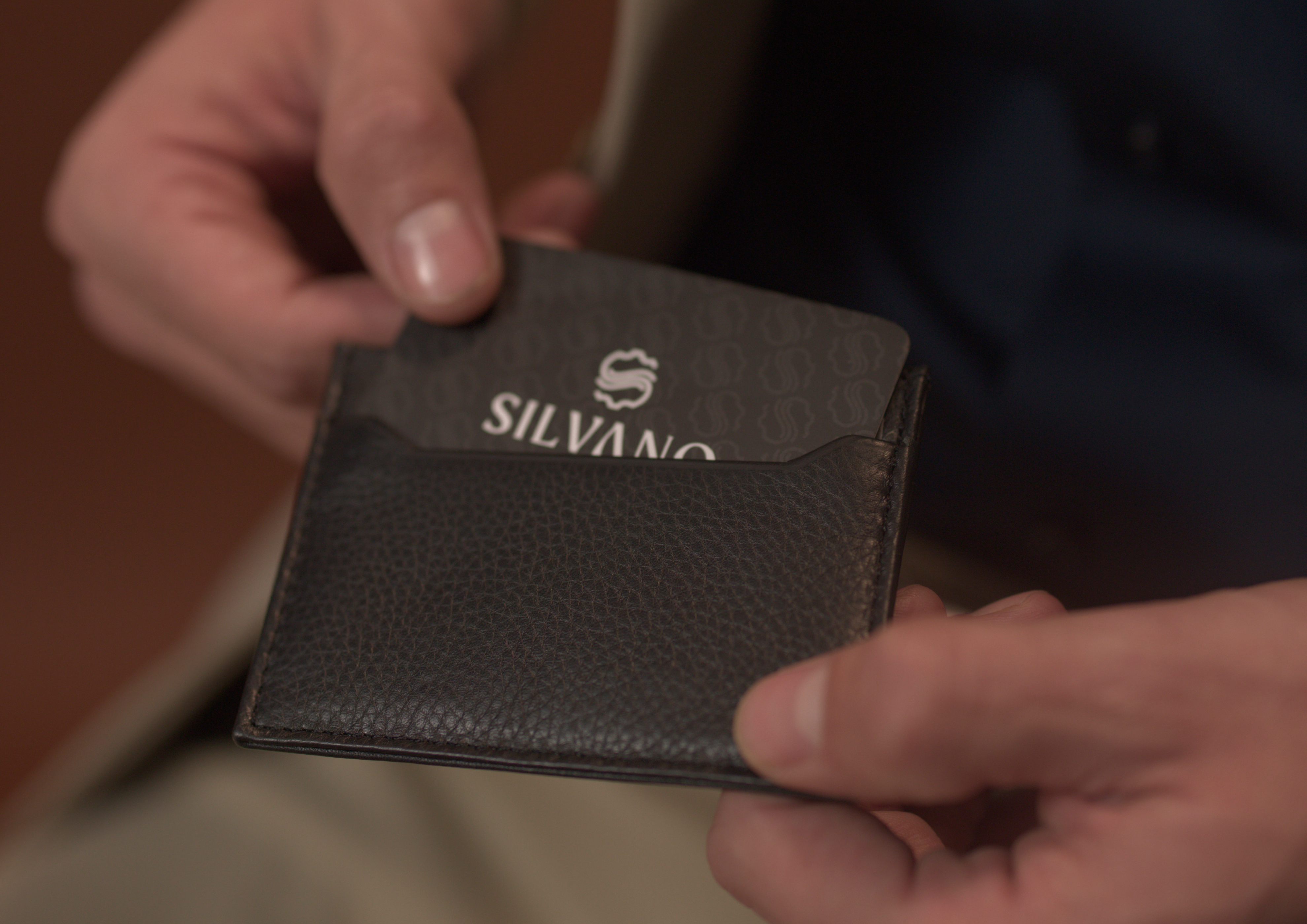 black leather card holder with silvano branding being used to insert a card