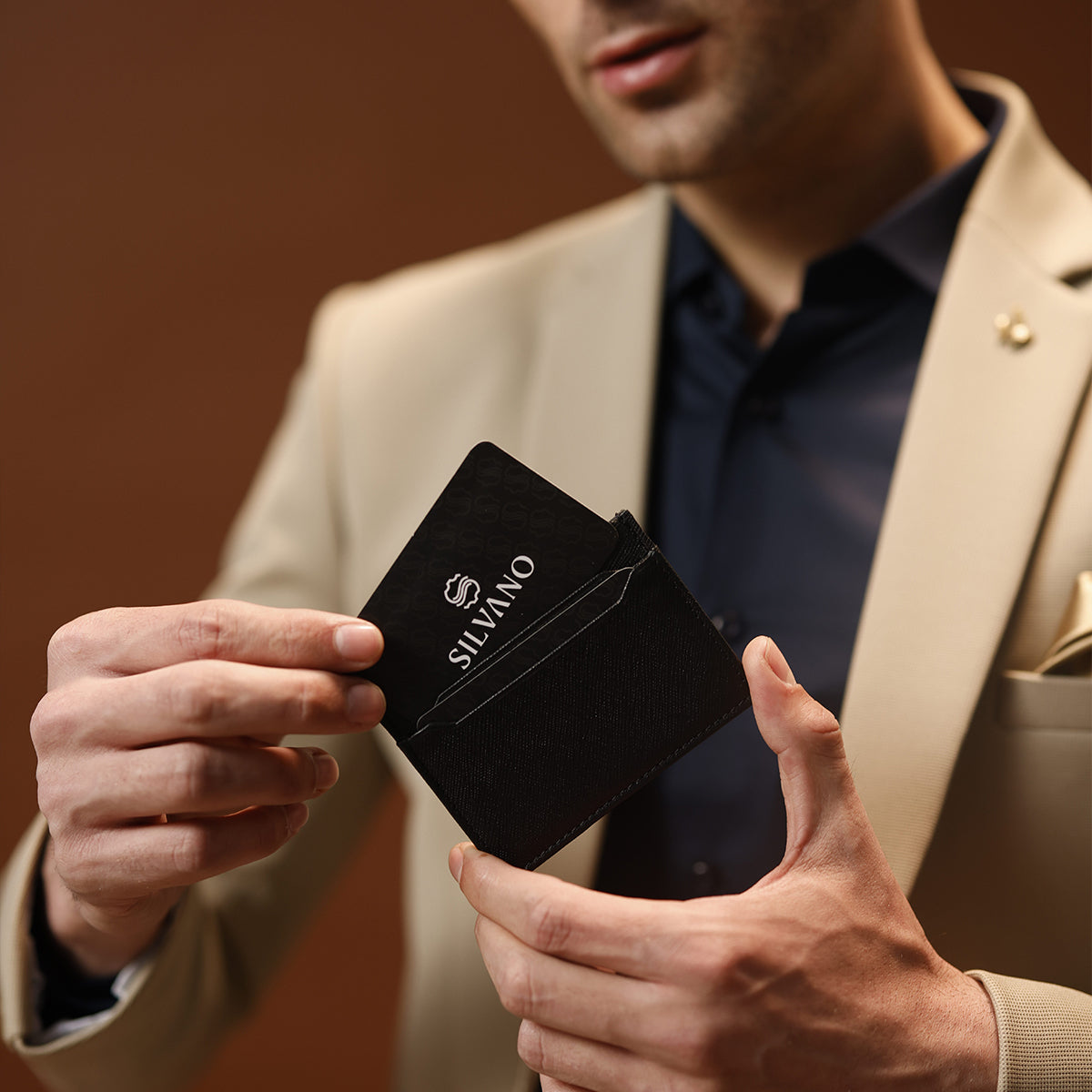 A stylish man in a beige blazer holding a sleek black Silvano card holder.